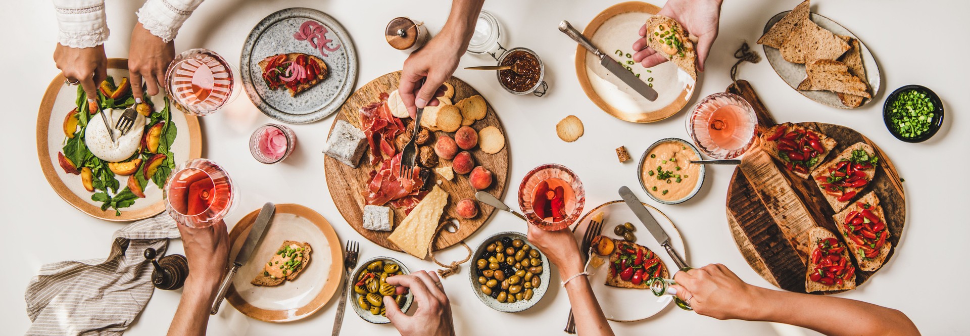 Peoples hands with rose wine and foods over various snacks table