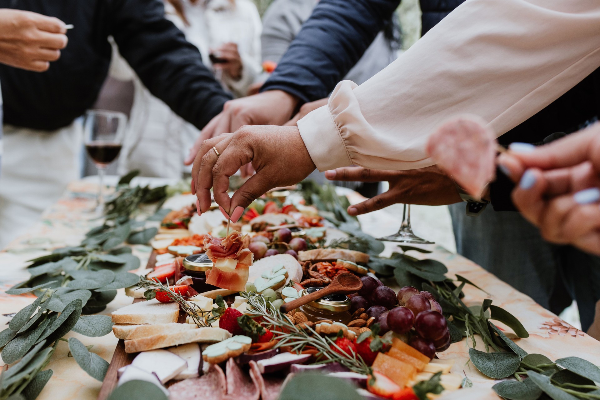hands and Outdoor charcuterie board with wine and cheese on wood table